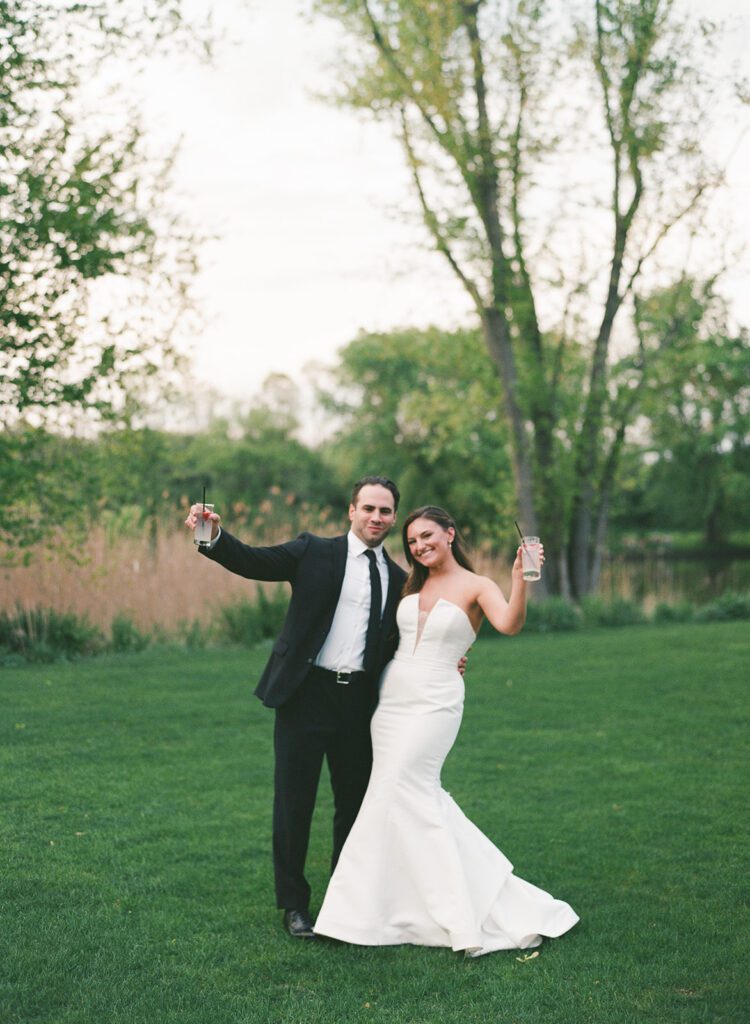 outdoor portrait of bride and groom holding up drinks and smiling