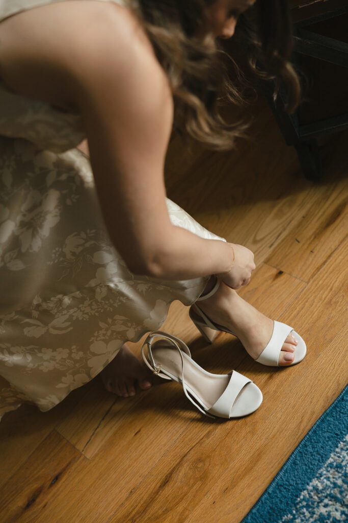 Bride slipping on white block-heeled sandals before her City Winery wedding.