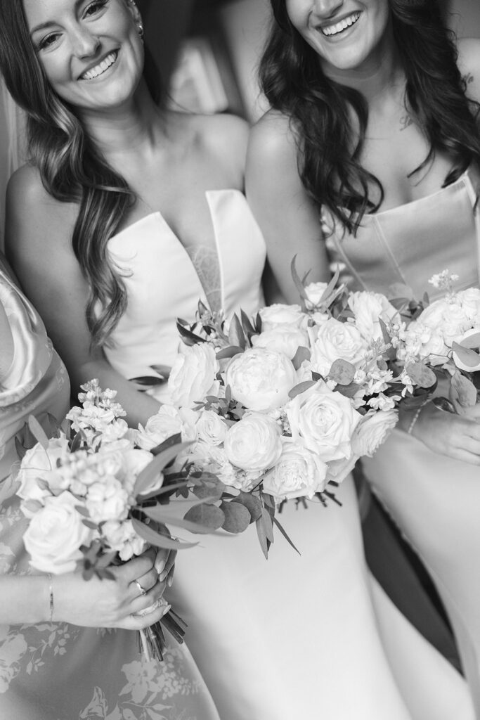 Black-and-white closeup of bride and bridesmaids laughing, bouquets in hand.
