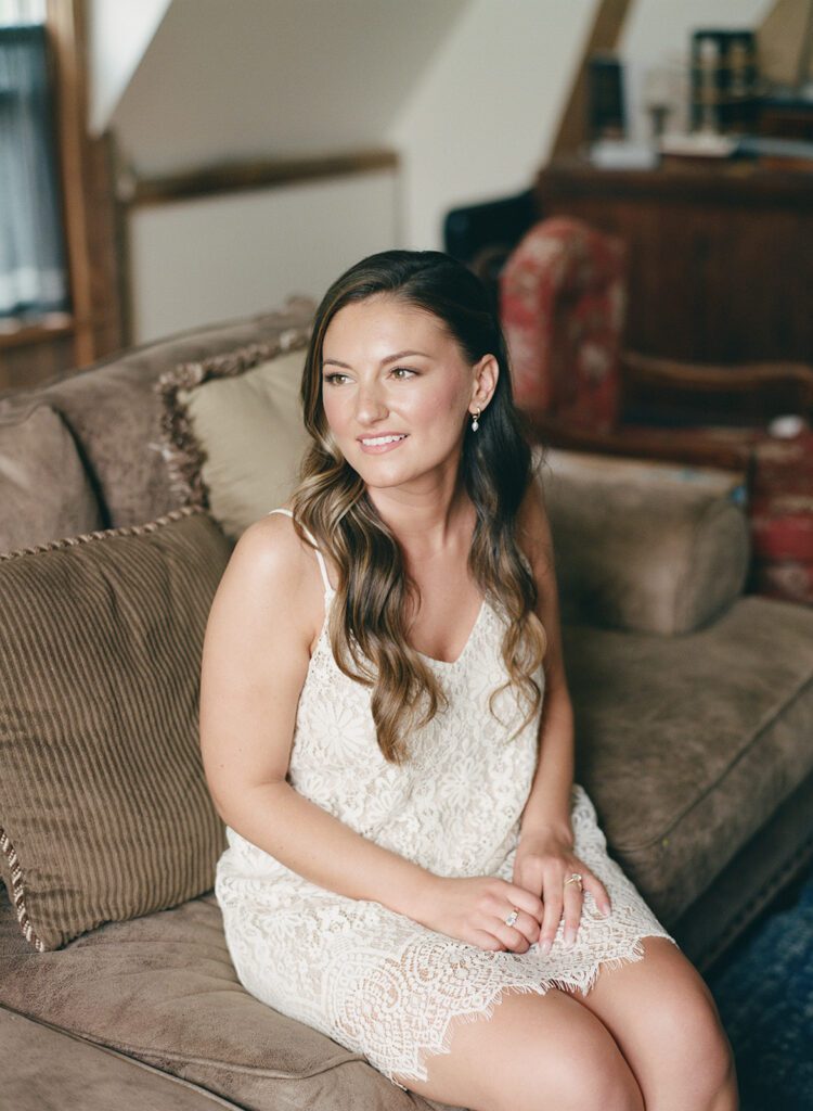 Bride in lace romper, seated and smiling softly during getting ready photos.