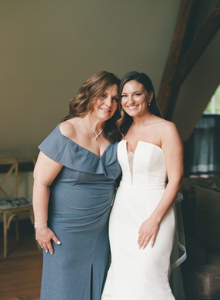 Bride posing with her mother in an elegant blue gown during wedding morning portraits.