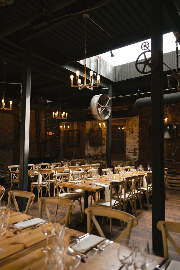 Reception space at City Winery with wooden tables, cross-back chairs, and glowing chandeliers hanging above.