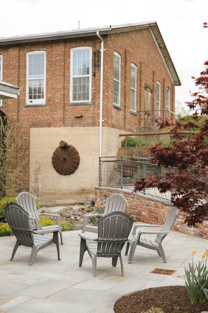 Outdoor patio with gray chairs at City Winery, surrounded by greenery and historic brick architecture.