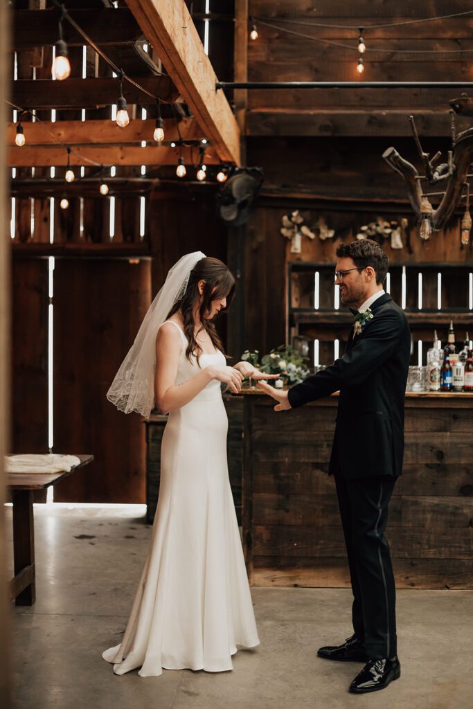 Bride and groom laugh together while looking at their new wedding rings in a rustic barn at The Arnold House.