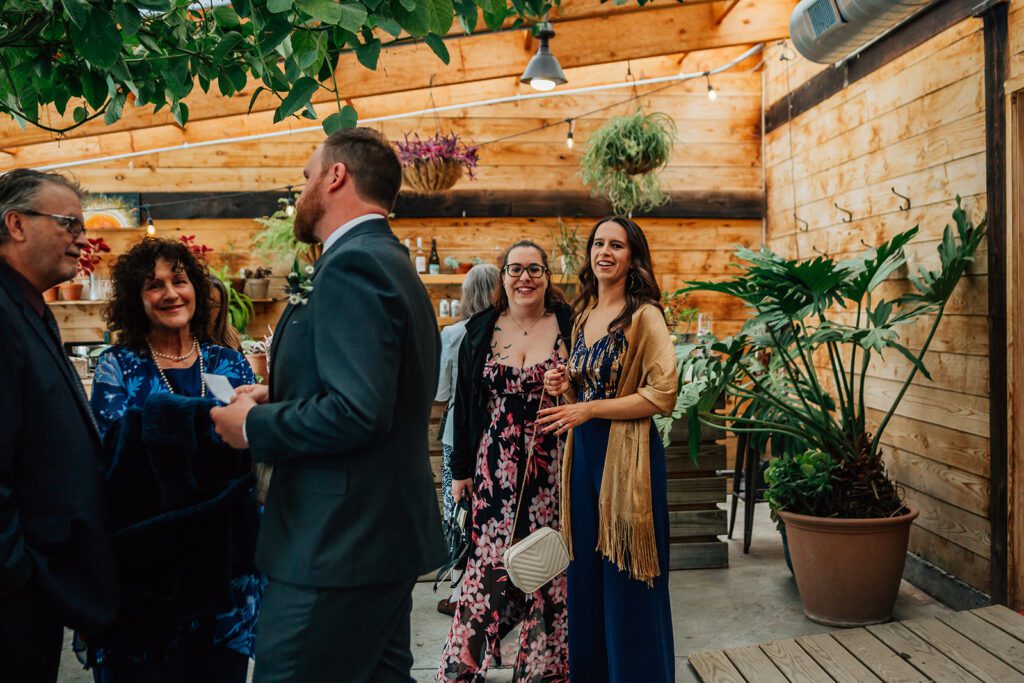 Guests mingle and chat under hanging plants inside The Arnold House greenhouse.