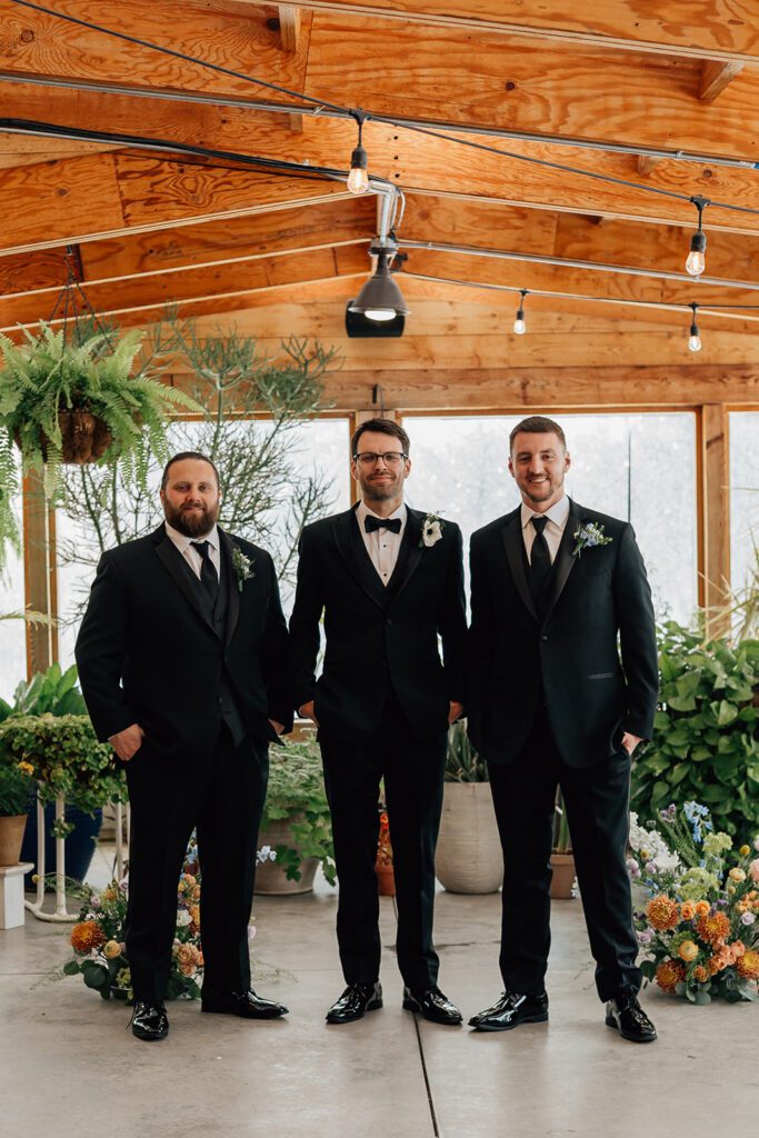 Groom with two groomsmen in black tuxedos posing indoors at The Arnold House.