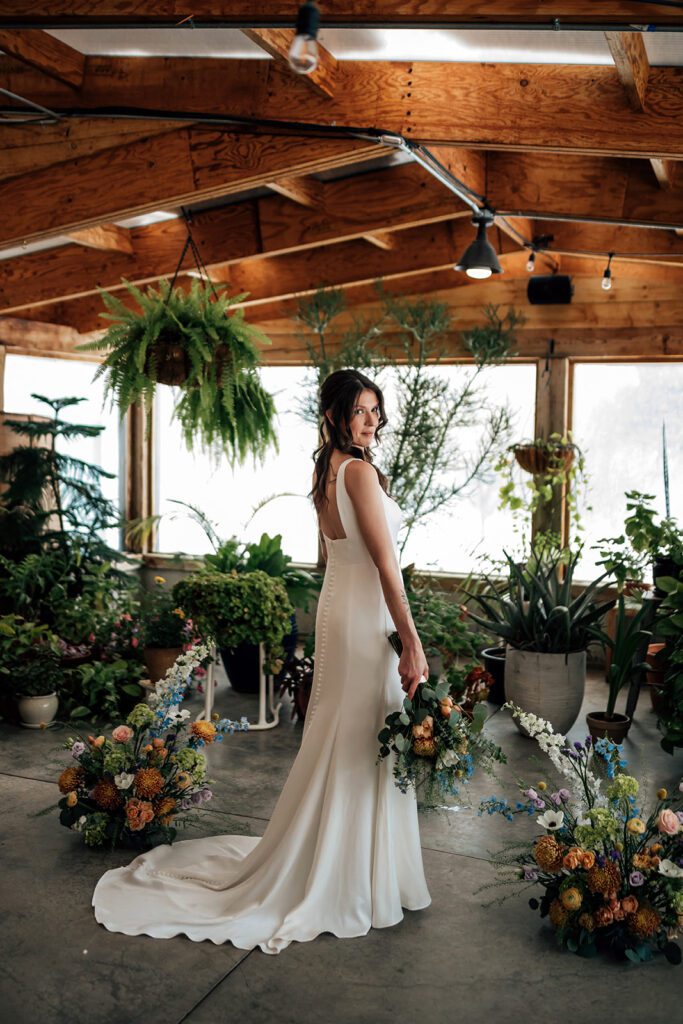 Bride poses with bouquet and trailing dress among lush greenery at The Arnold House.