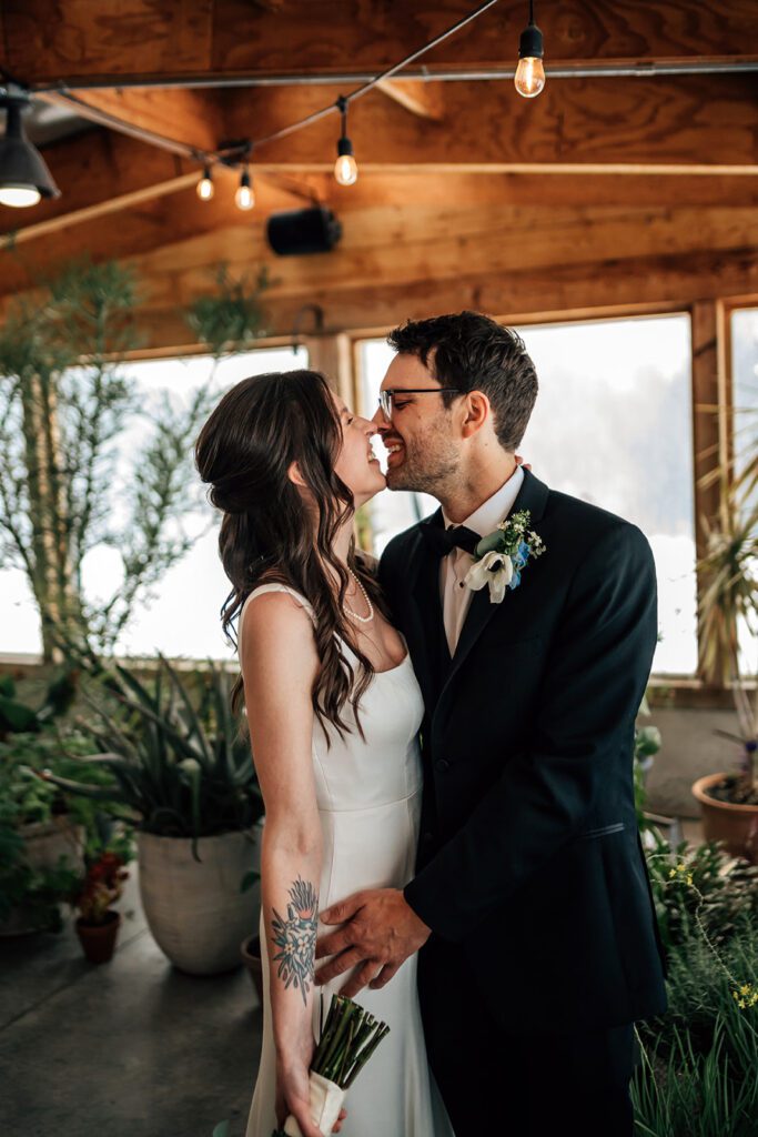 Bride and groom laugh, nearly kissing, holding hands in a plant-filled room at The Arnold House.