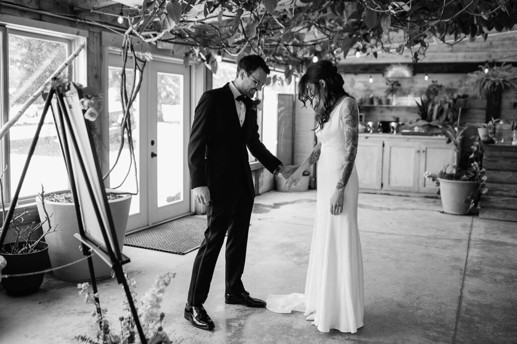Bride and groom share an emotional first look, holding hands under hanging vines.