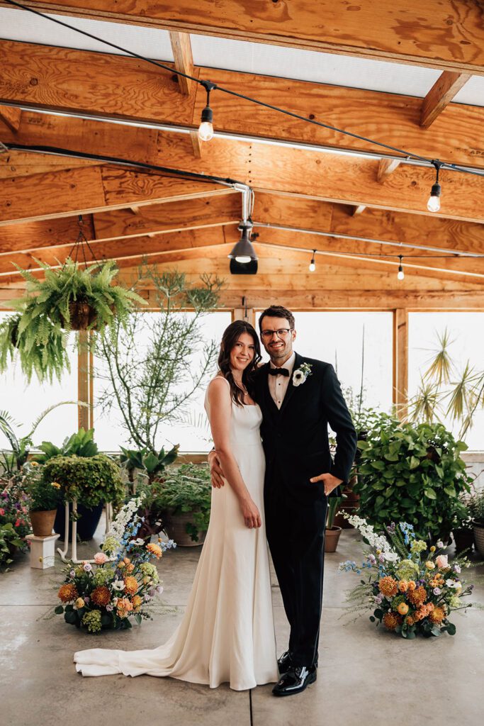 Bride and groom pose together surrounded by plants and flowers at The Arnold House.