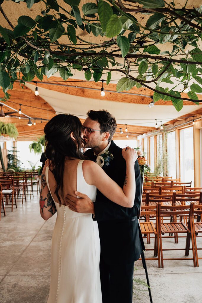Bride and groom share a kiss under hanging vines in the ceremony space at The Arnold House.