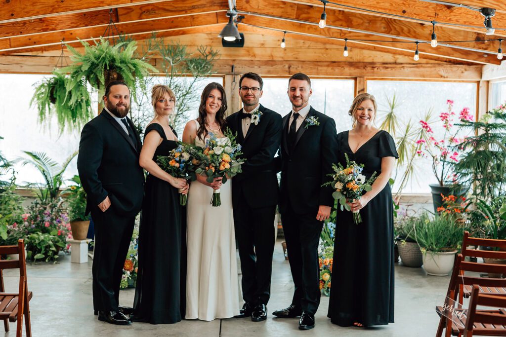Wedding party poses indoors at The Arnold House with lush plants and colorful bouquets.