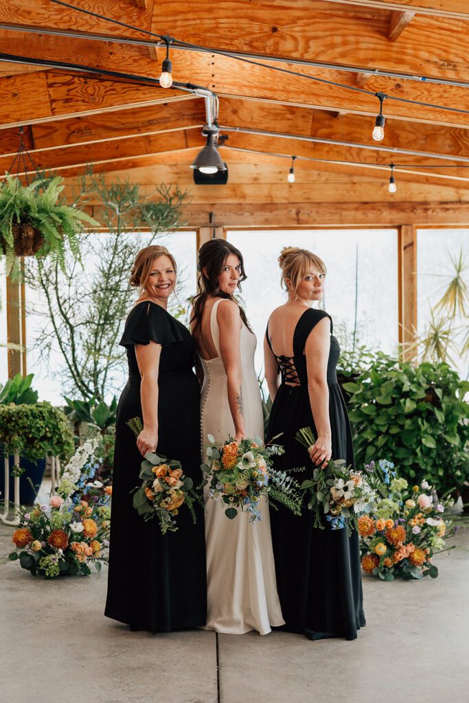 Bride with two bridesmaids in black dresses, holding bouquets, posing indoors at The Arnold House.