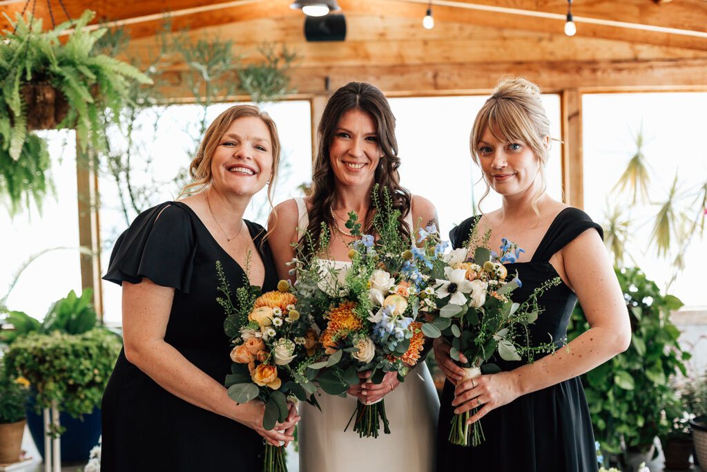 Bride with bridesmaids smiling, holding bouquets of colorful flowers at The Arnold House.
