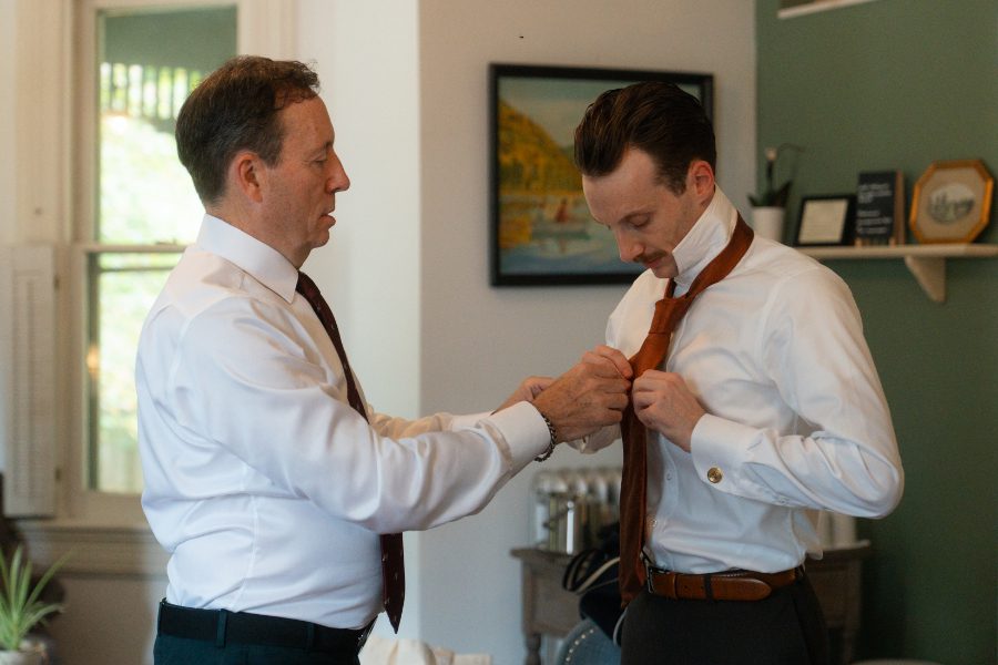 grooms father helping with his tie.