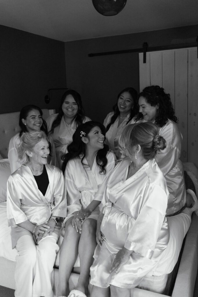 bride sitting on a bed with her bridesmaids. all wearing sink robes.