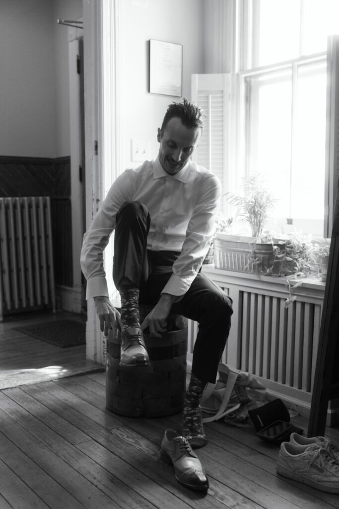 black and white photo of groom putting on his brown wedding shoes
