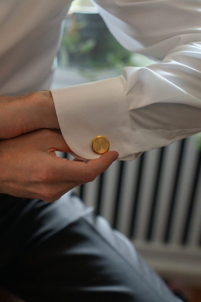 close up of groom putting gold cufflinks on