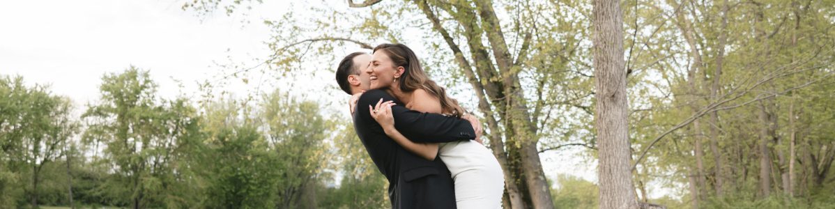 Bride and groom embrace by a peaceful riverside with trees and soft greenery, capturing a joyful, candid moment often seen in destination weddings in Hudson Valley.