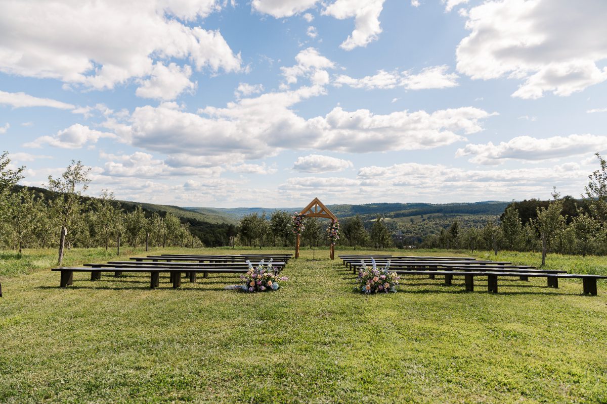 Outdoor ceremony setup at Seminary Hill with wooden benches and floral accents, overlooking rolling hills and orchards—an idyllic backdrop for destination weddings in Hudson Valley.