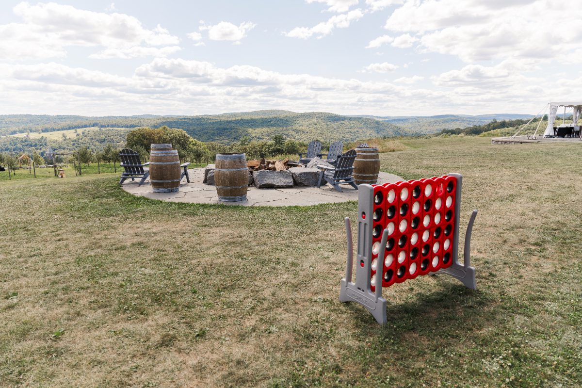 Outdoor lounge area at Seminary Hill with Adirondack chairs, wine barrels, and lawn games, set against panoramic views perfect for destination weddings in Hudson Valley.