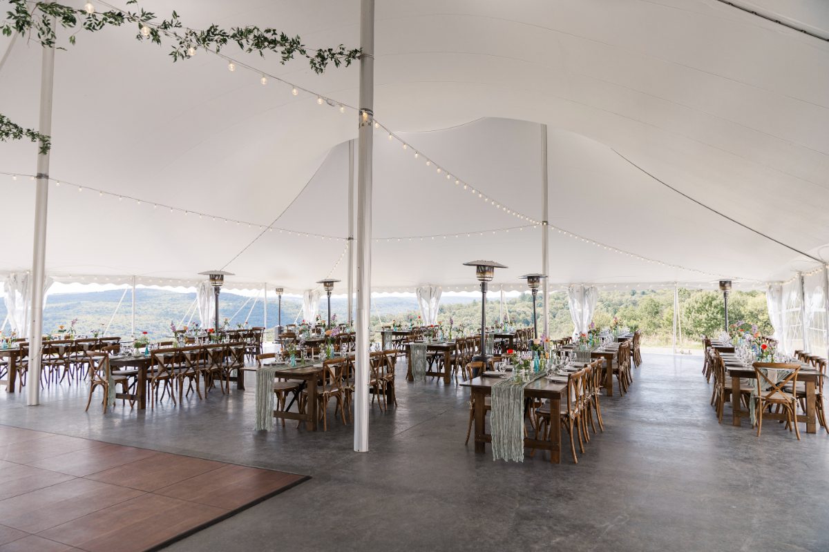 Open-air reception tent at Seminary Hill with long wooden tables, string lights, and sweeping mountain views, creating an elevated setting for destination weddings in Hudson Valley.