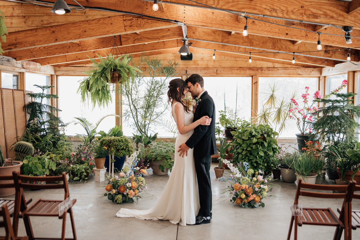 Bride and groom share a quiet moment surrounded by plants and florals in a sunlit greenhouse at The Arnold House, a unique backdrop for destination weddings in Hudson Valley.