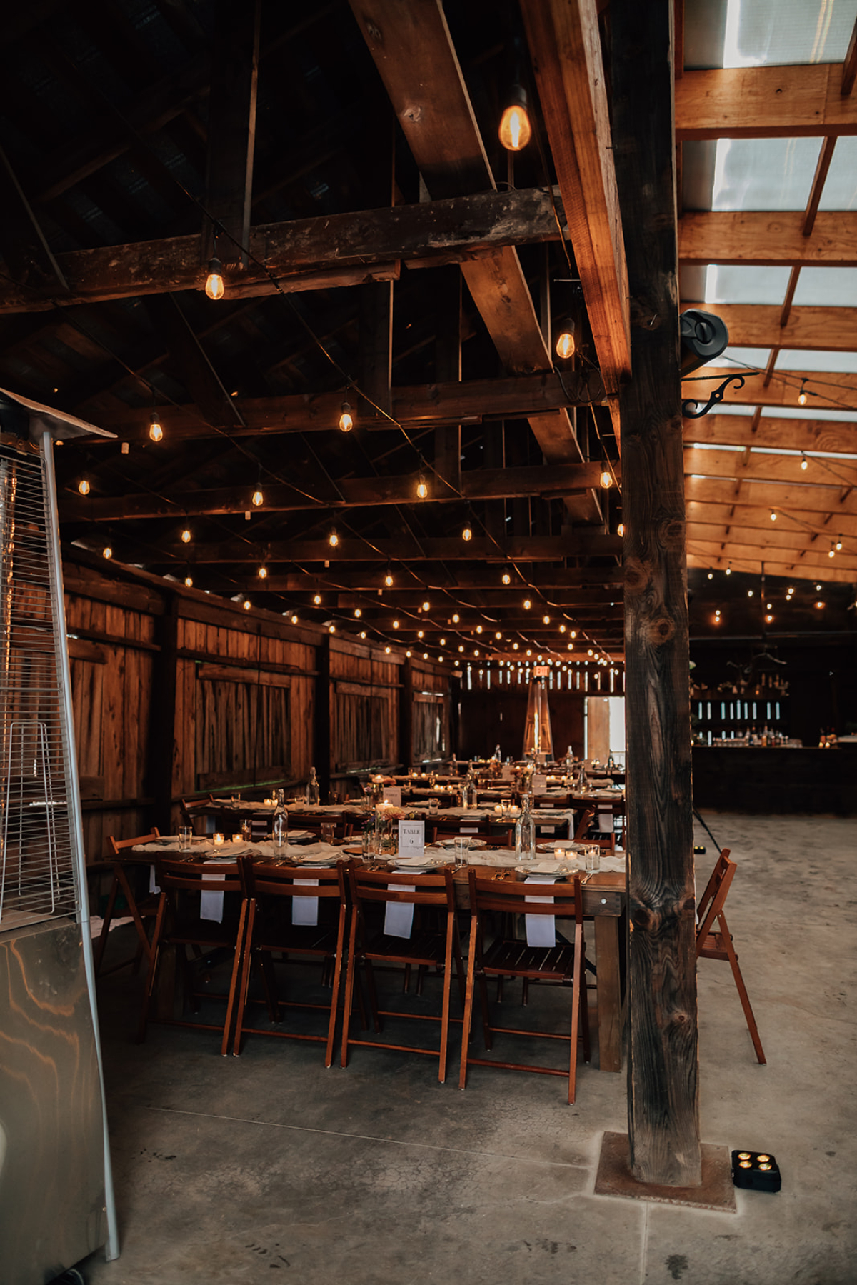 Warm, rustic reception space at The Arnold House with long wooden tables, string lights, and exposed beams, creating an intimate setting for destination weddings in Hudson Valley.