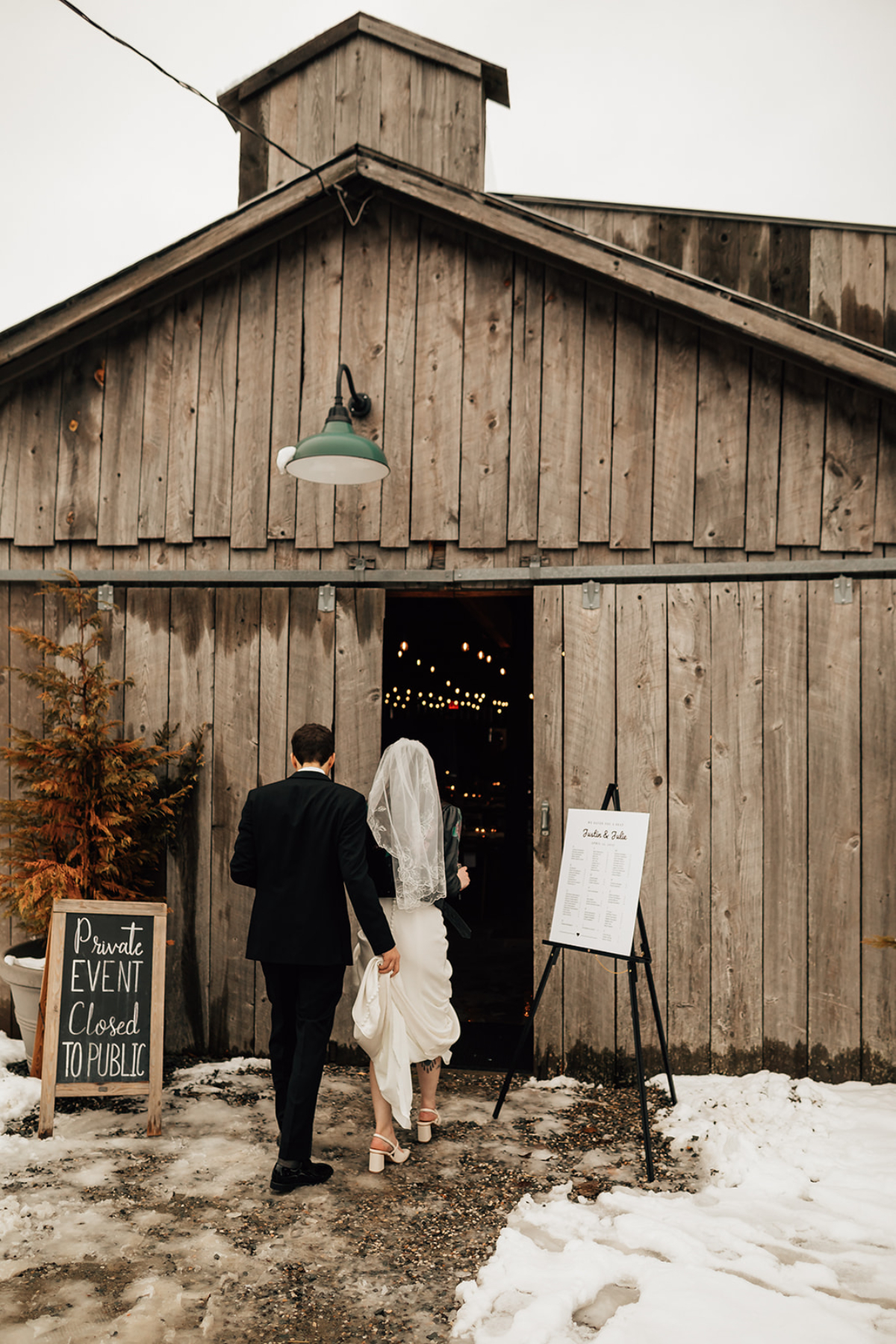 Couple enters a barn-style venue at The Arnold House in winter, with snow on the ground and soft lighting inside, capturing the charm of destination weddings in Hudson Valley year-round.