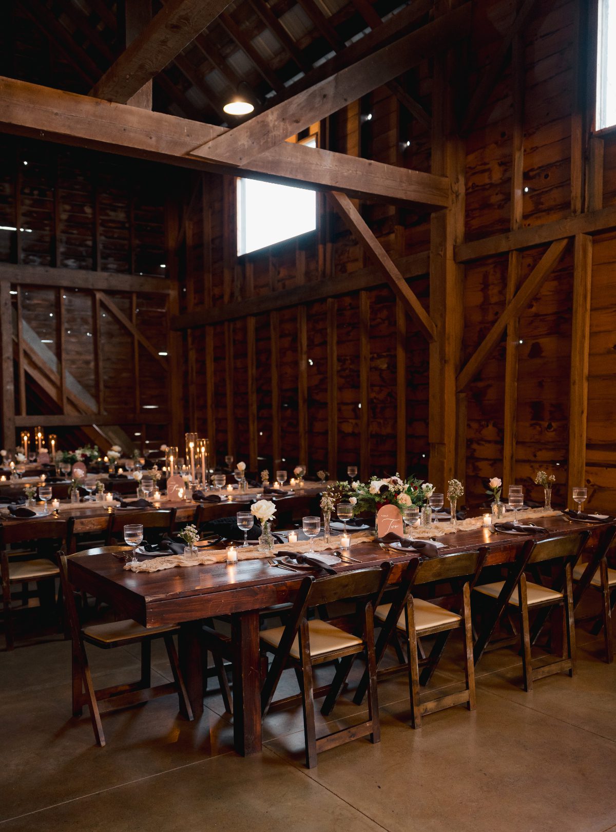 Rustic barn reception at The Barn on Hubbard with exposed wood beams, long tables, candlelight, and floral details for destination weddings in Hudson Valley.