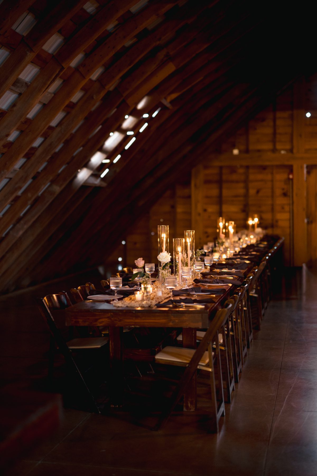 Long candlelit reception table inside The Barn on Hubbard, set beneath a warm wooden ceiling with soft florals and intimate lighting.