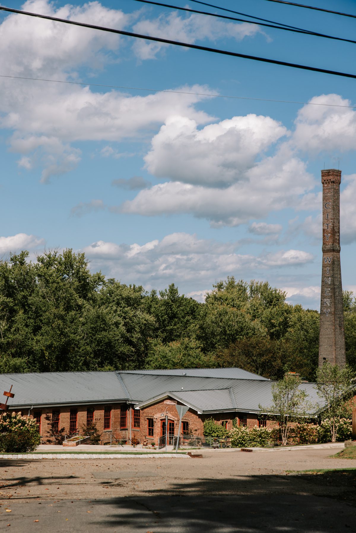 Wide view of City Winery grounds with restored brick buildings and iconic smokestack, showcasing the scenic, industrial-chic setting ideal for destination weddings in Hudson Valley.