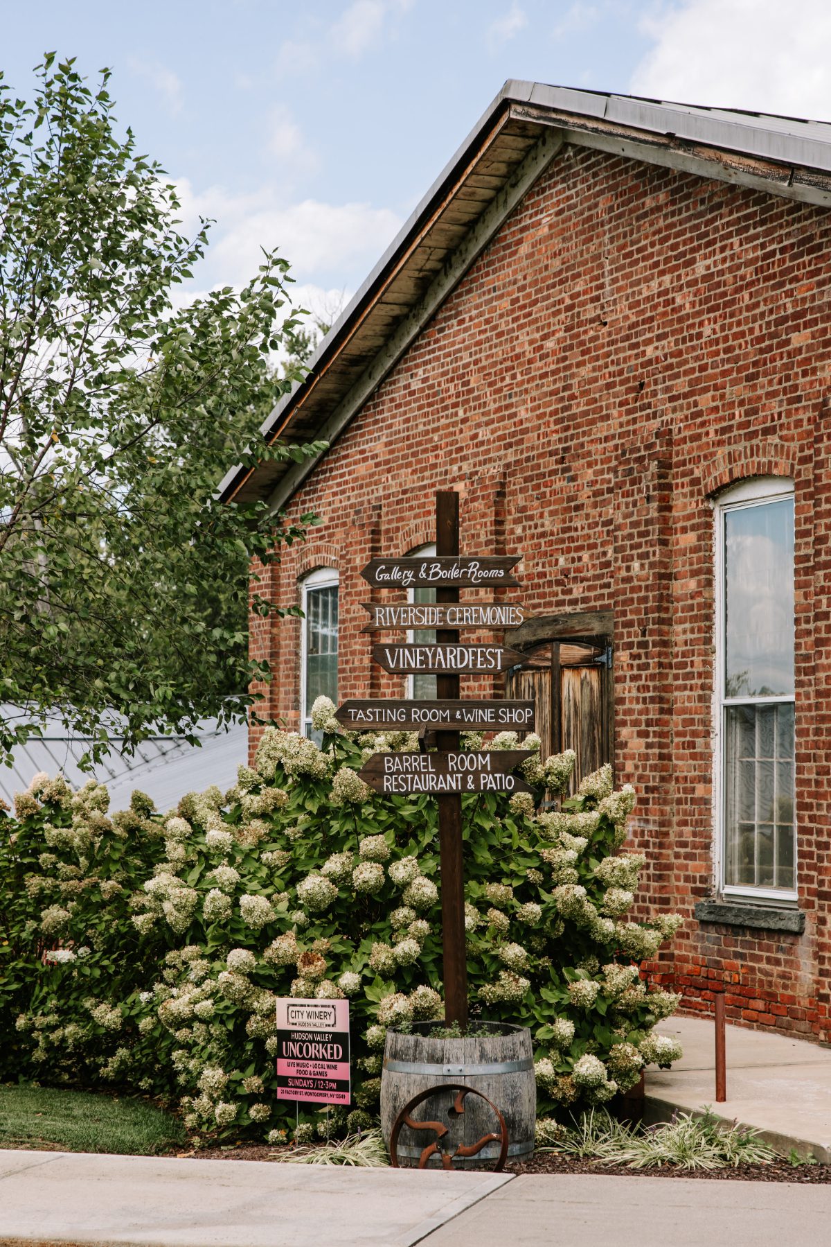 Brick exterior at City Winery with directional signage for ceremonies, tastings, and events, surrounded by hydrangeas—an inviting setting often chosen for destination weddings in Hudson Valley.