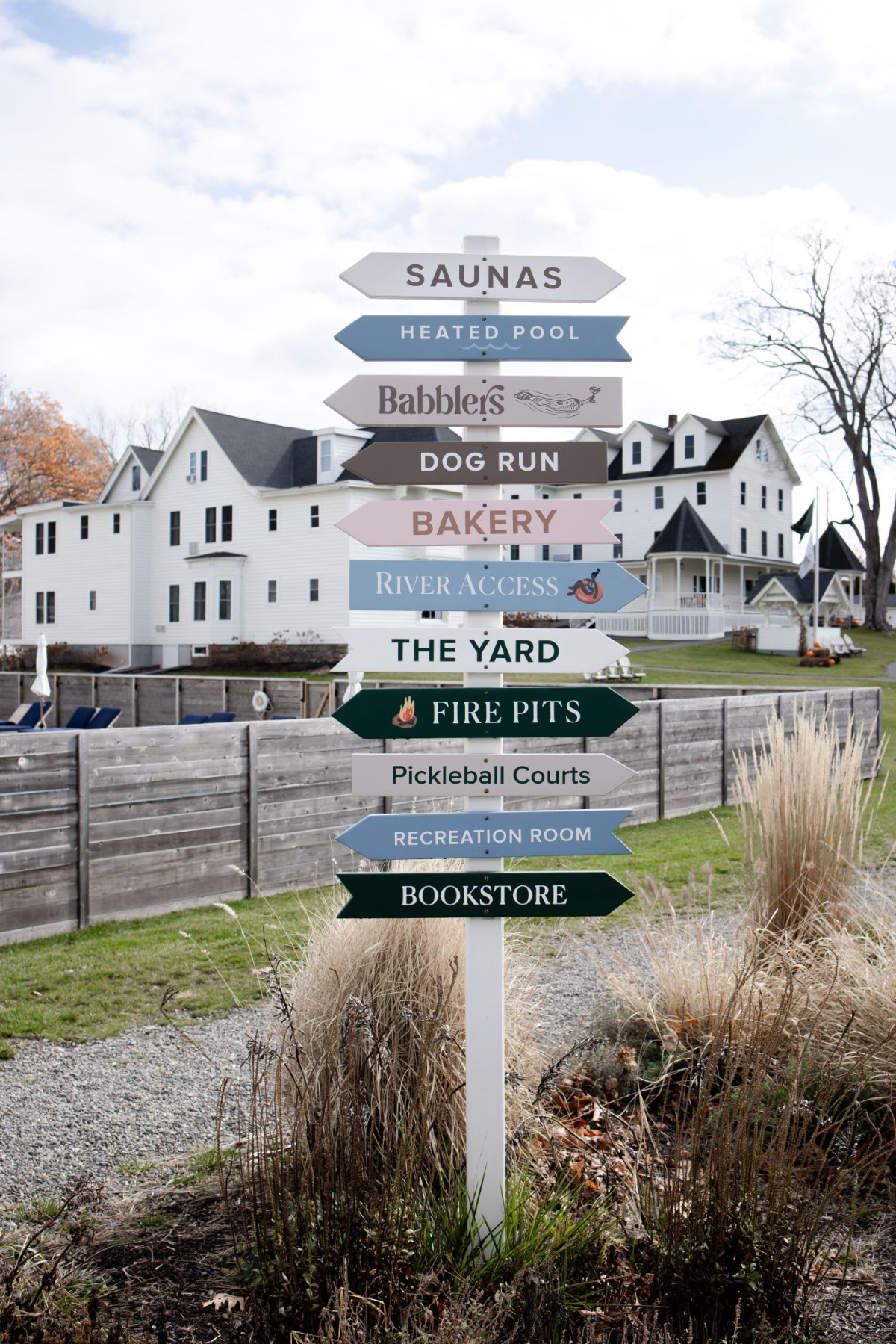 Directional signpost at Wylder at Windham listing amenities like spa, bakery, and fire pits, with resort buildings in the background for destination weddings in Hudson Valley.