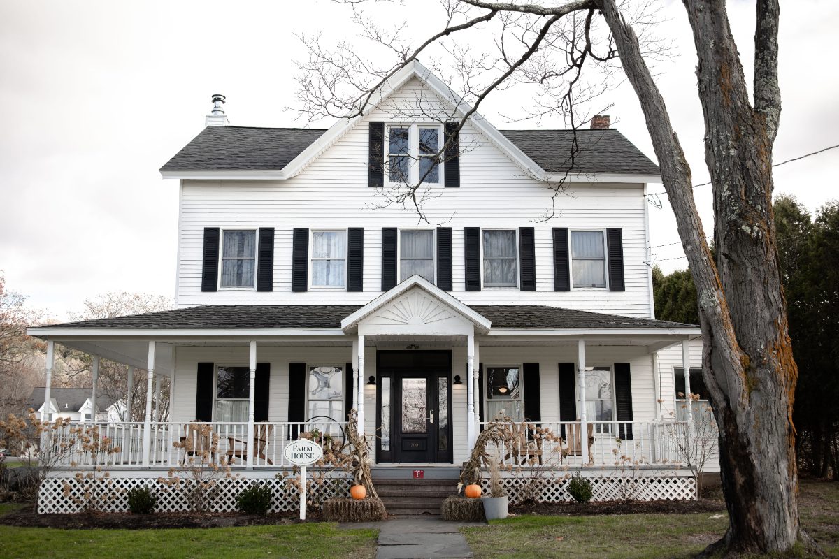White farmhouse exterior at Wylder at Windham with black shutters, front porch, and rustic fall decor, creating a cozy, welcoming space for destination weddings in Hudson Valley.