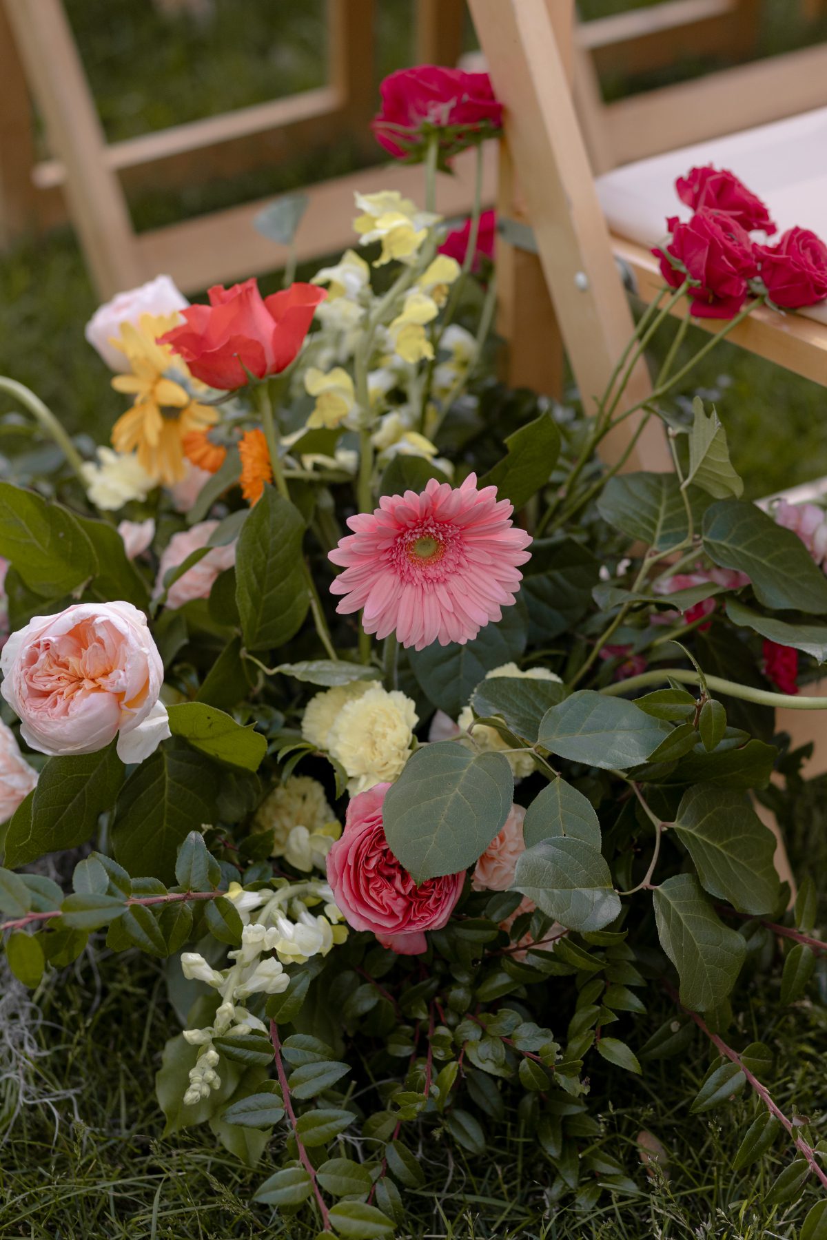 Colorful floral arrangement with roses, daisies, and greenery placed beside wooden chairs, adding a vibrant detail often seen in destination weddings in Hudson Valley.