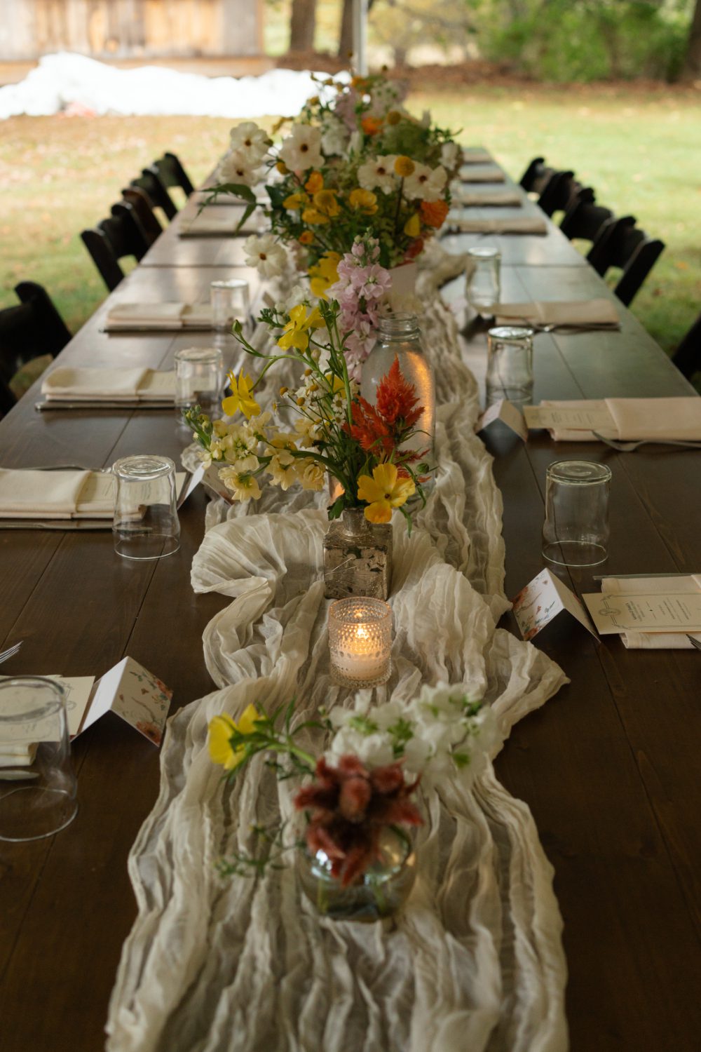 A long wooden table is decorated with colorful floral arrangements, soft candles, and textured linens. The intimate, nature‑inspired design embodies the thoughtful, handcrafted aesthetic often seen at Hudson Valley micro weddings.