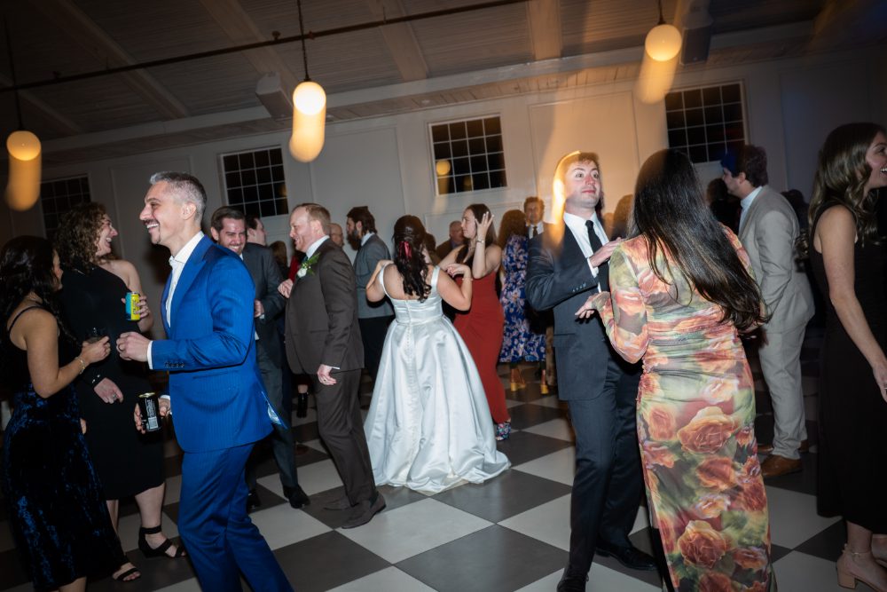 Wedding guests dance together on the black-and-white checkered dance floor at Audrey’s Farmhouse during December wedding.