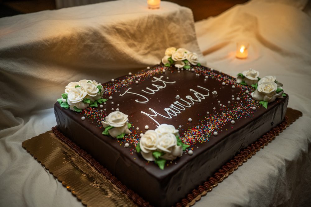 A rectangular chocolate wedding cake decorated with white frosting roses, colorful sprinkles, and "Just Married" lettering at an Audrey's Farmhouse wedding reception.