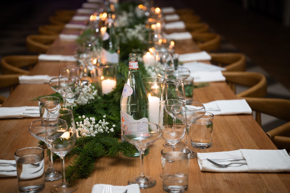 Long wooden reception table decorated with lush greenery, candles, and glassware for a winter Hudson Valley wedding.
