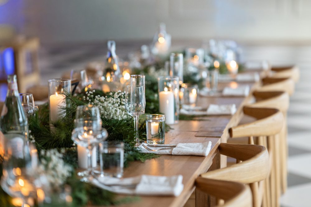 Long wooden reception tables decorated with lush greenery, candles, and glassware for a winter Hudson Valley wedding.